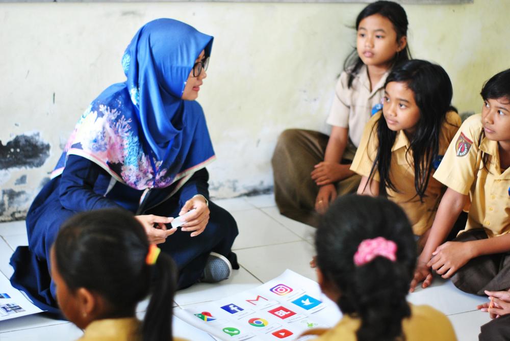 Woman and schoolgirls sit on the floor for lessons.